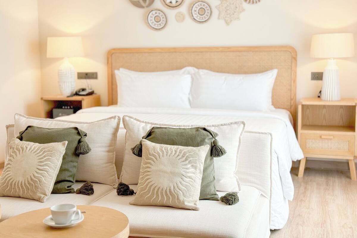 A neatly arranged hotel room with a bed, two bedside tables, and a round table with a cup.