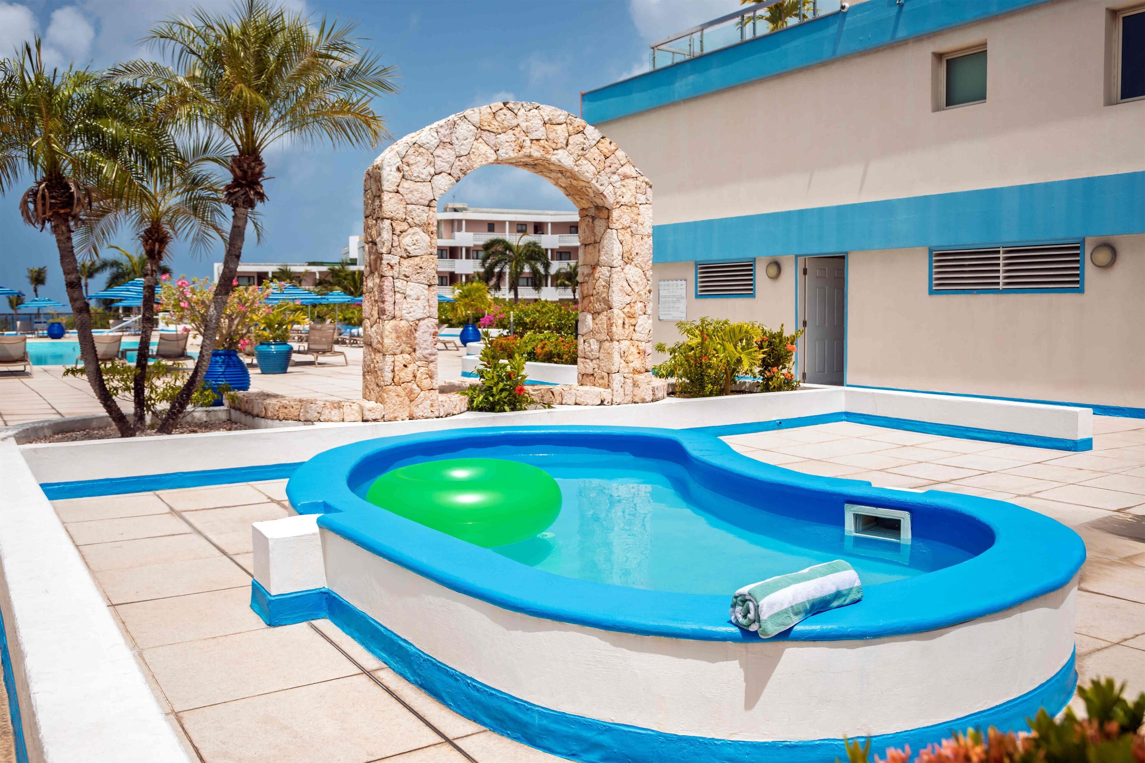 A swimming pool with a stone archway, surrounded by palm trees and lounge chairs.