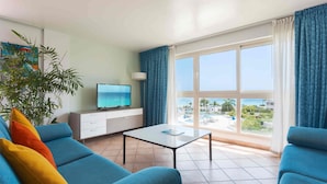 En moderne stue med sofa, sofabord, fjernsyn og et stort vindue med udsigt over et resort.