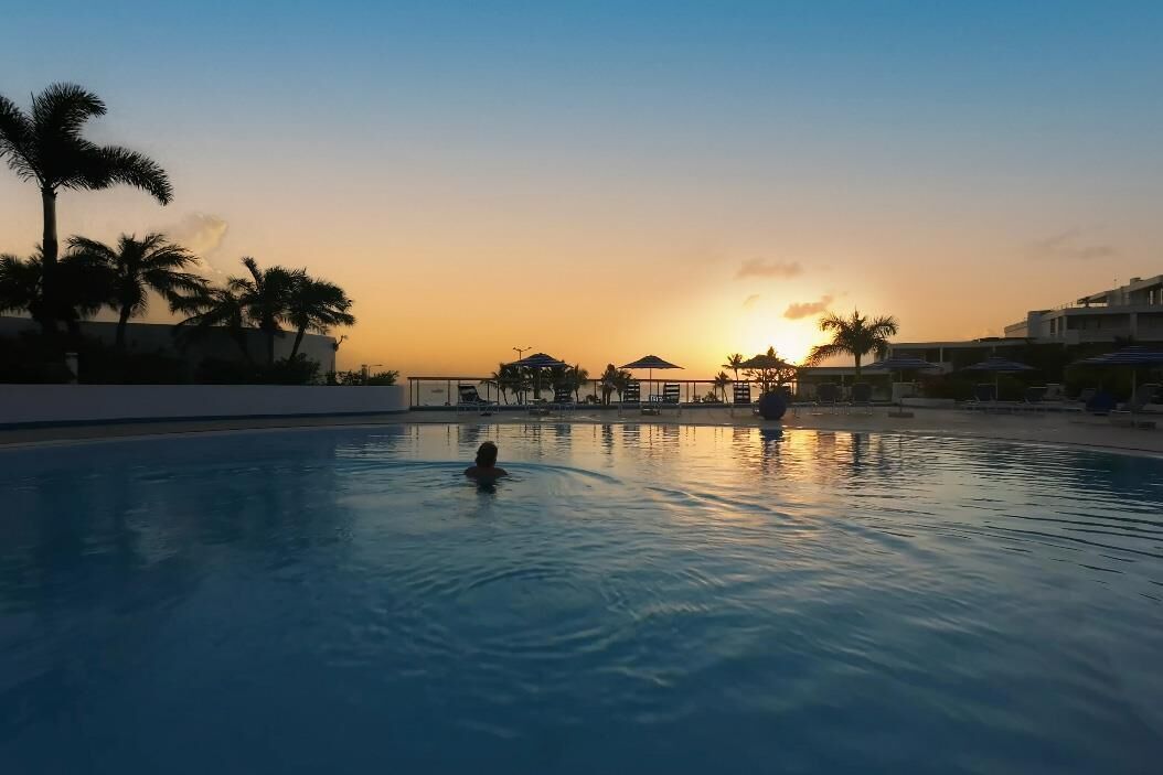 Una piscina al atardecer con palmeras y un edificio en el fondo.