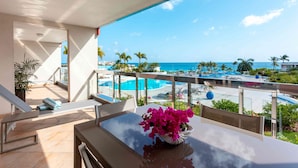 En balkon med udsigt over pool og strand, et bord med en vase blomster og en stol.
