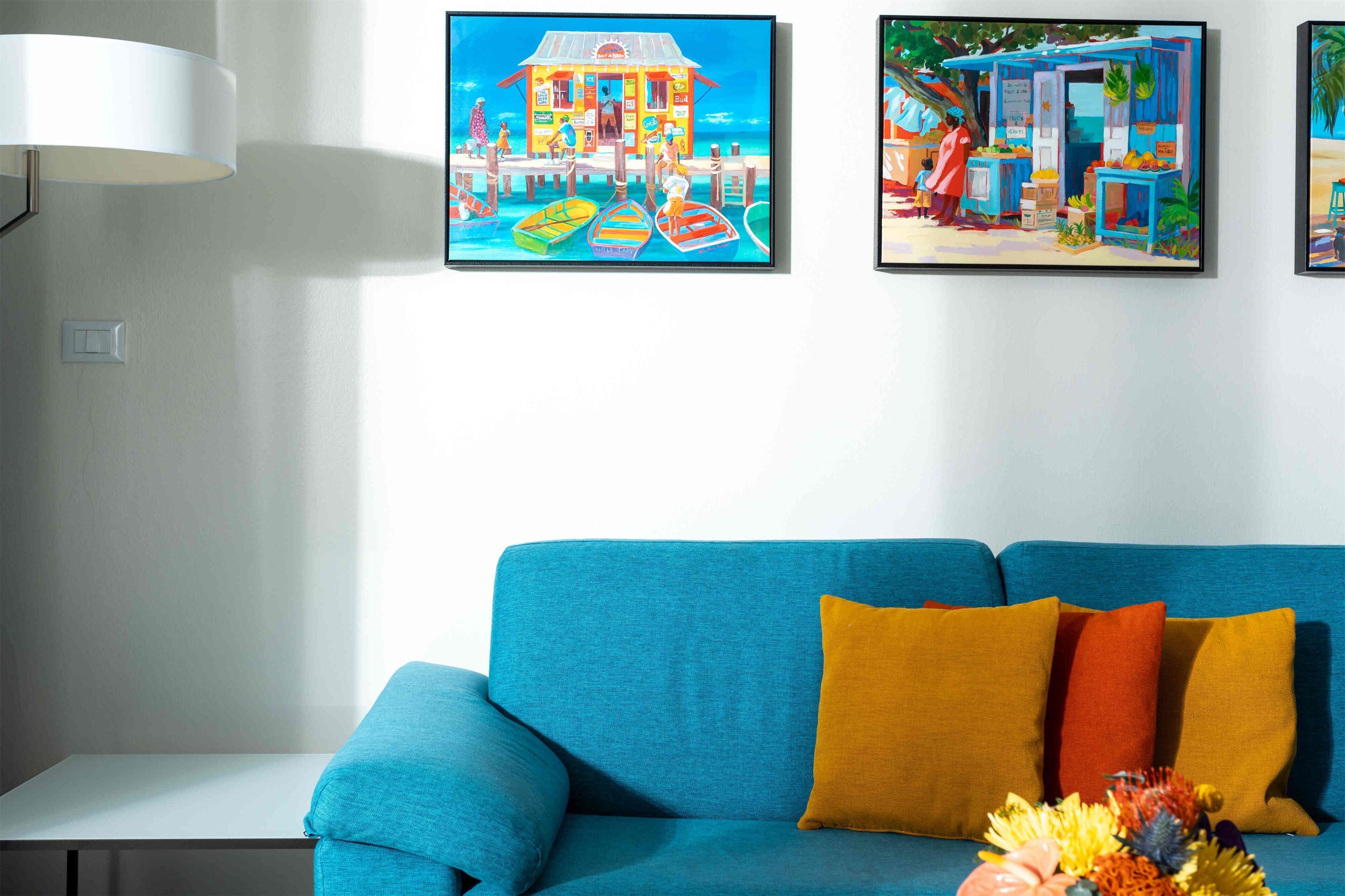 A room with a blue sofa, a white table, and two colorful paintings on the wall.