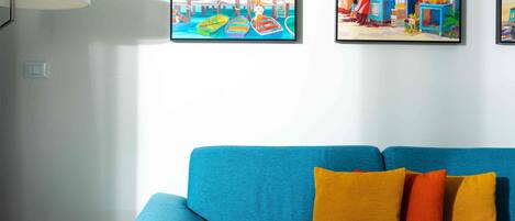 A room with a blue sofa, a white table, and two colorful paintings on the wall.
