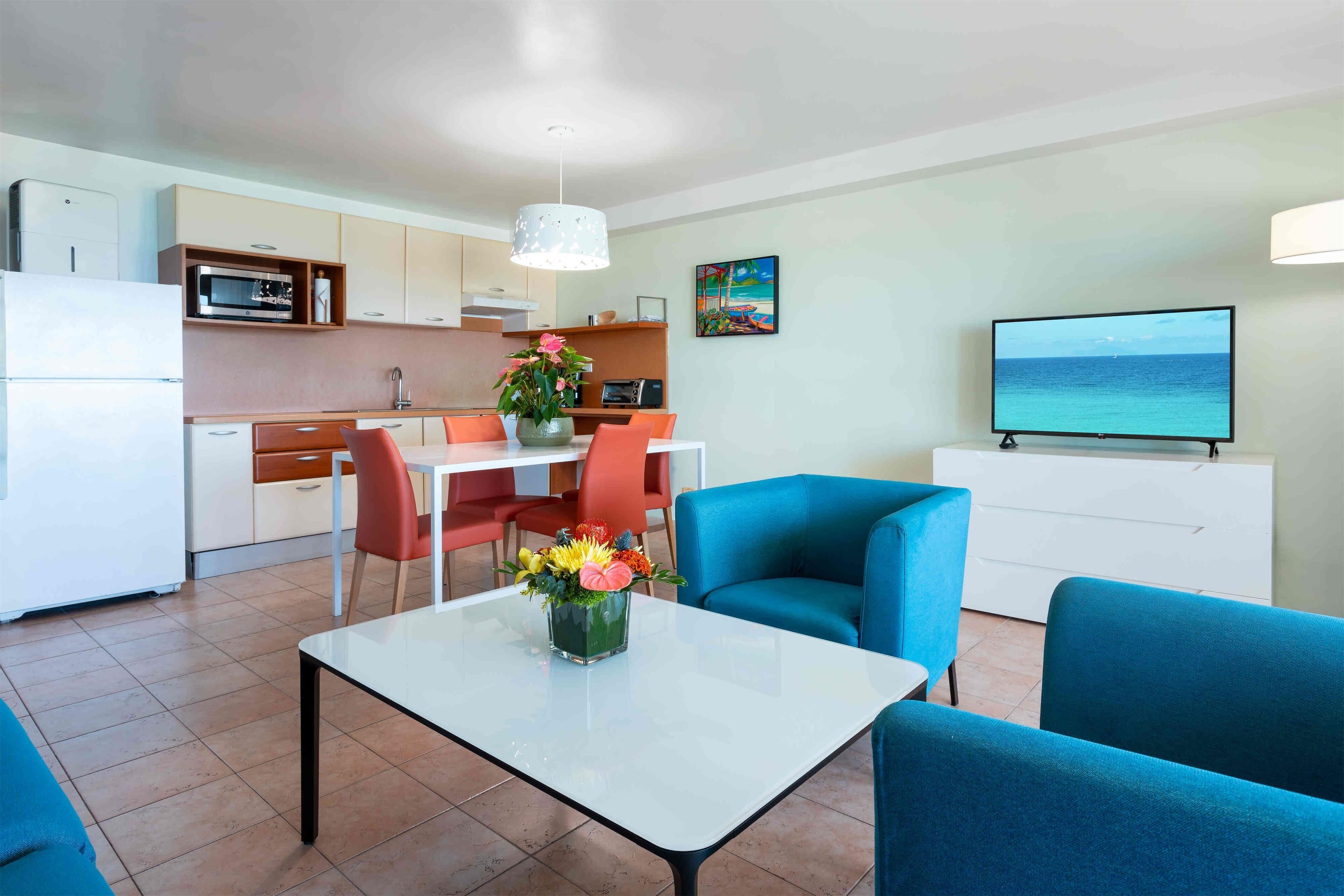 A modern living room with a dining area, kitchen, and a TV displaying a scenic view.