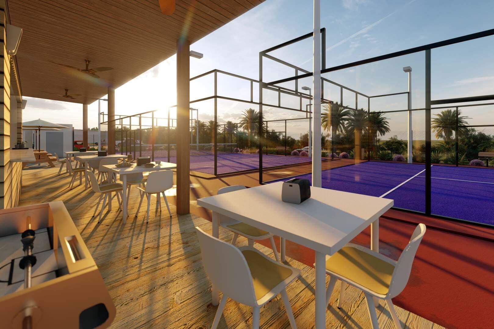 Un área de estar al aire libre con mesas y sillas, una cancha de tenis visible a través de grandes ventanales y una terraza de madera.