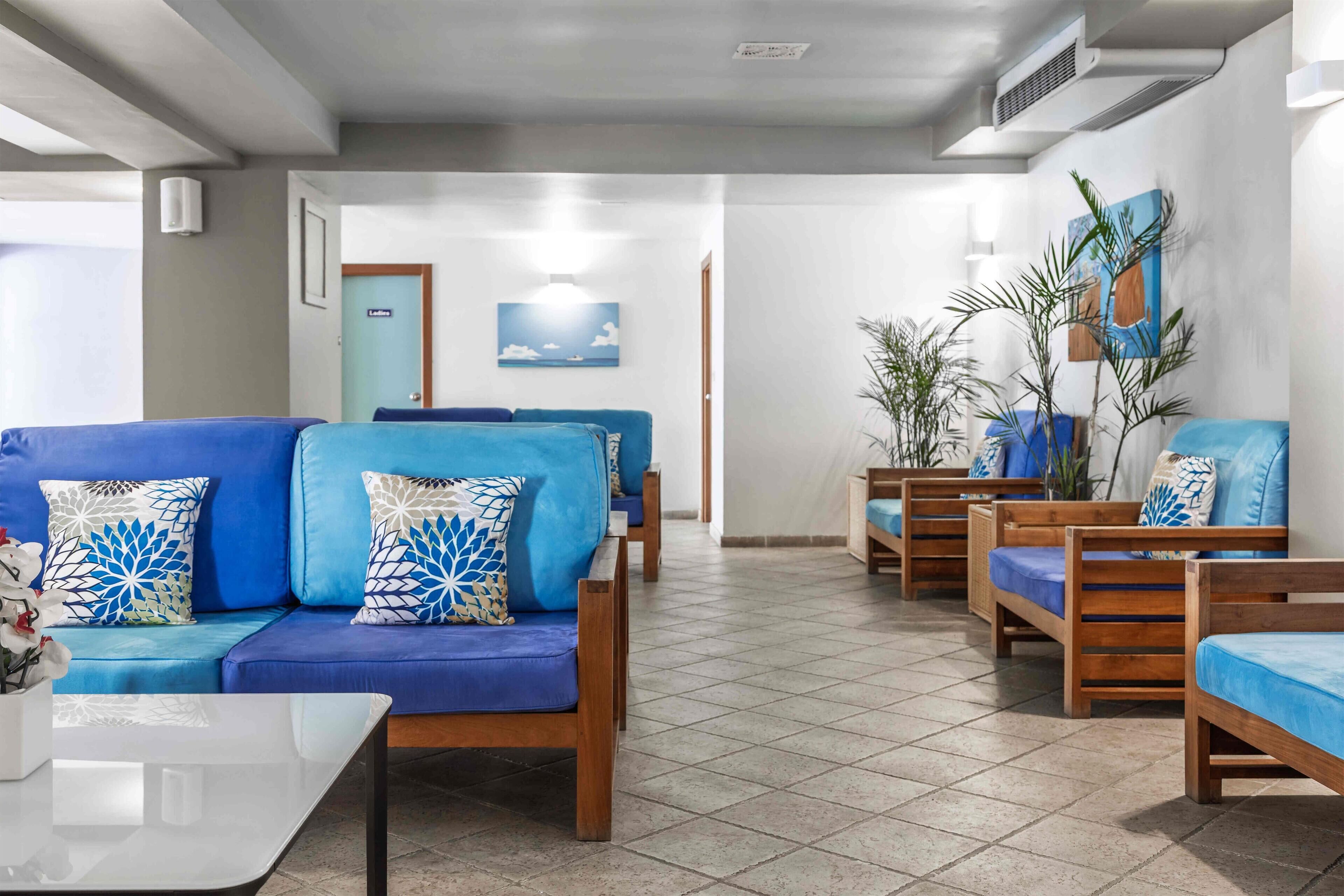Un moderno vestíbulo de hotel con un conjunto de sofá azul, bancos de madera y piso de baldosas.