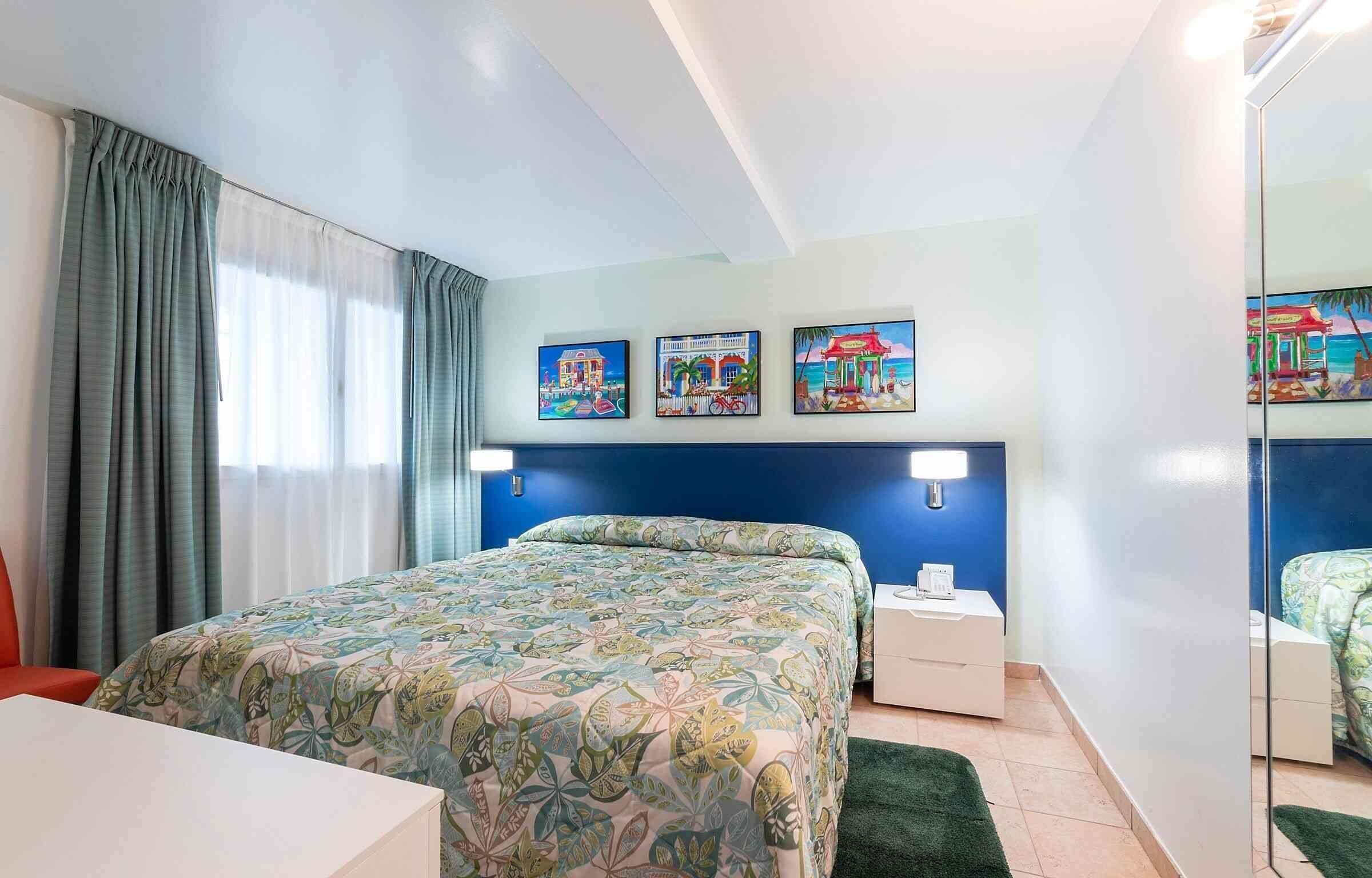 Ein Hotelzimmer mit Bett, Nachttisch, Spiegel und drei Bildern an der Wand.