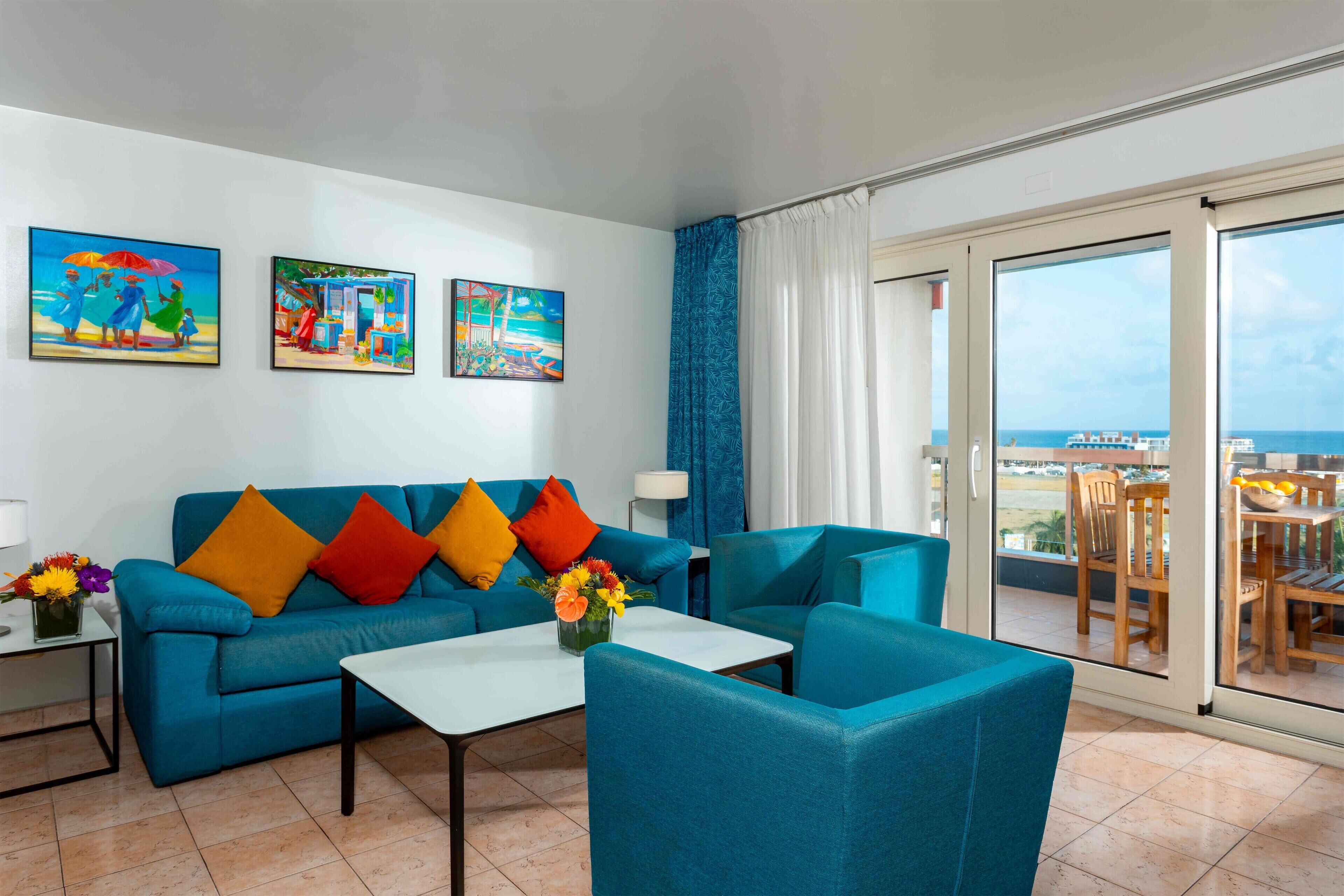 Una sala de estar moderna con un sofá azul, una mesa de centro y un balcón con vista al mar.