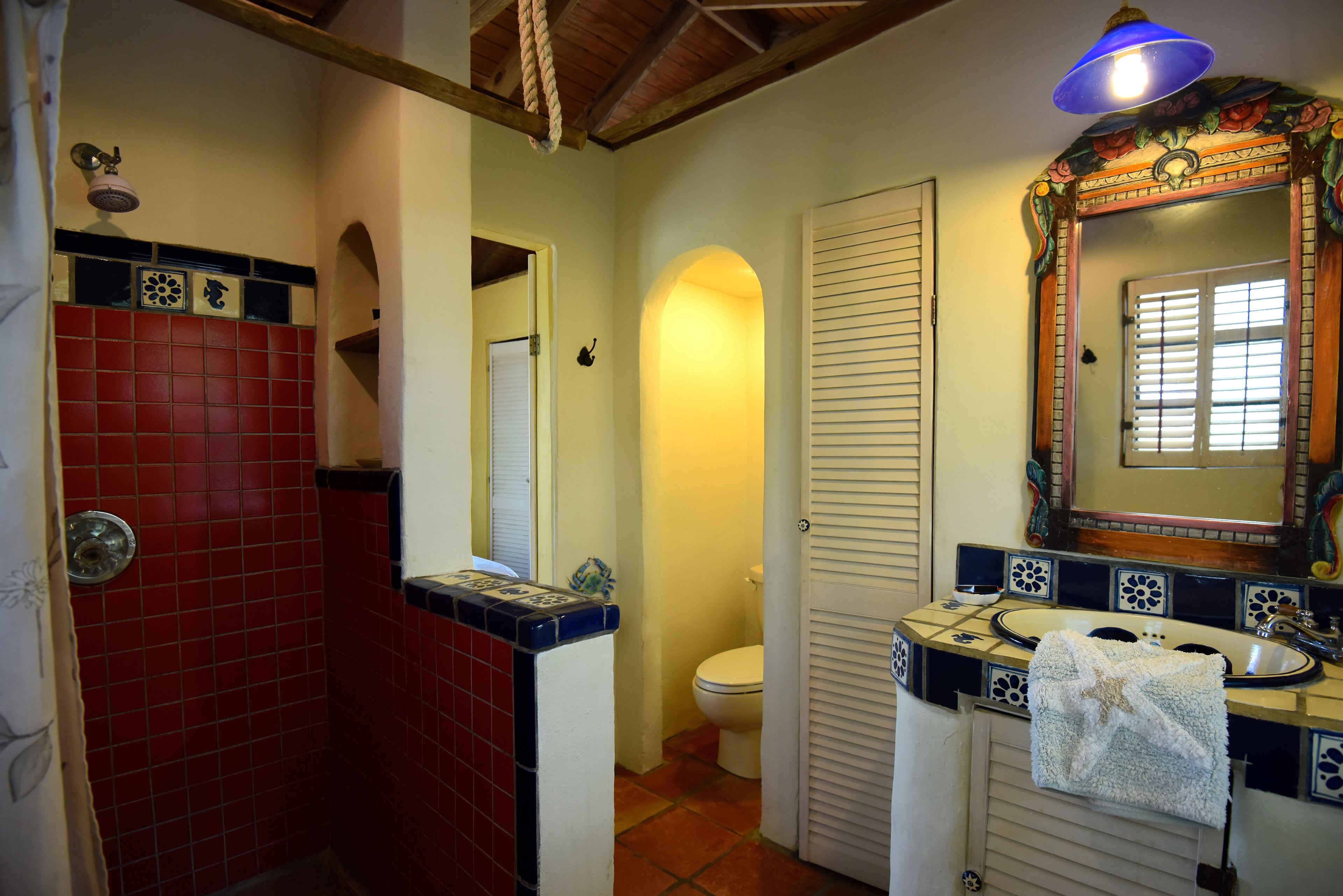 A bathroom with a red-tiled shower area, a white toilet, and a sink with a decorative mirror.