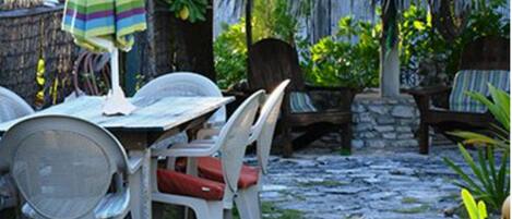 Un espace extérieur aménagé avec des sièges, un toit de chaume, des chaises en plastique et un parasol à rayures.