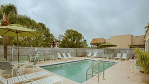 Zona de piscina amb gandules i ombrelles, envoltada per una tanca de fusta i arbres.