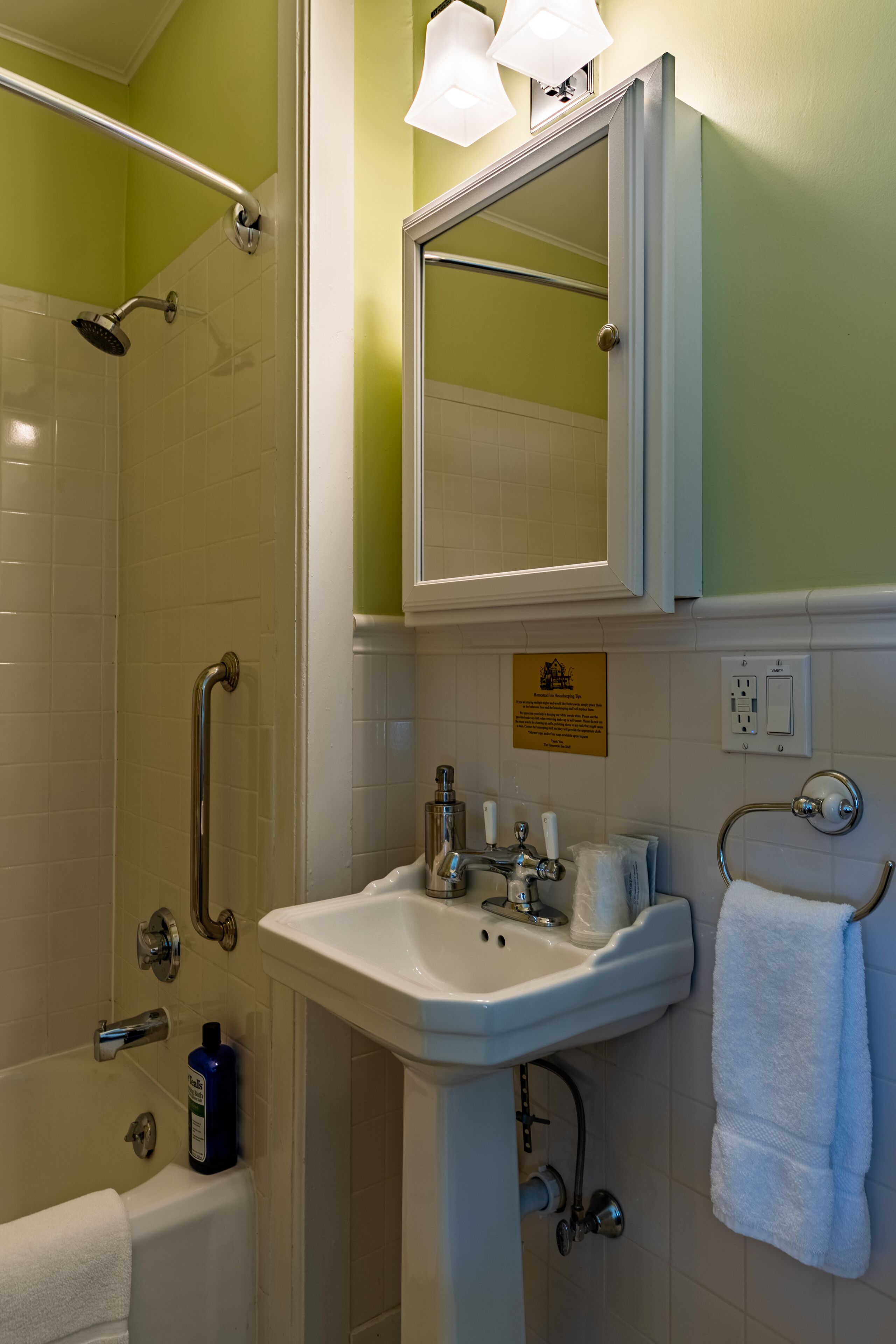 A bathroom with a shower, grab bars, a sink, and a mirror.