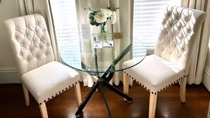 A corner room with two white upholstered chairs, a glass table, and a vase with white flowers. - Homestead Inn (New Milford)