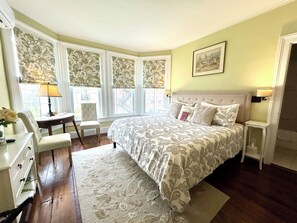 A bedroom with a large bed, a desk, a chair, and a window with curtains. - Homestead Inn (New Milford)