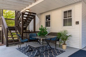 A covered patio with a staircase, outdoor furniture, and potted plants.