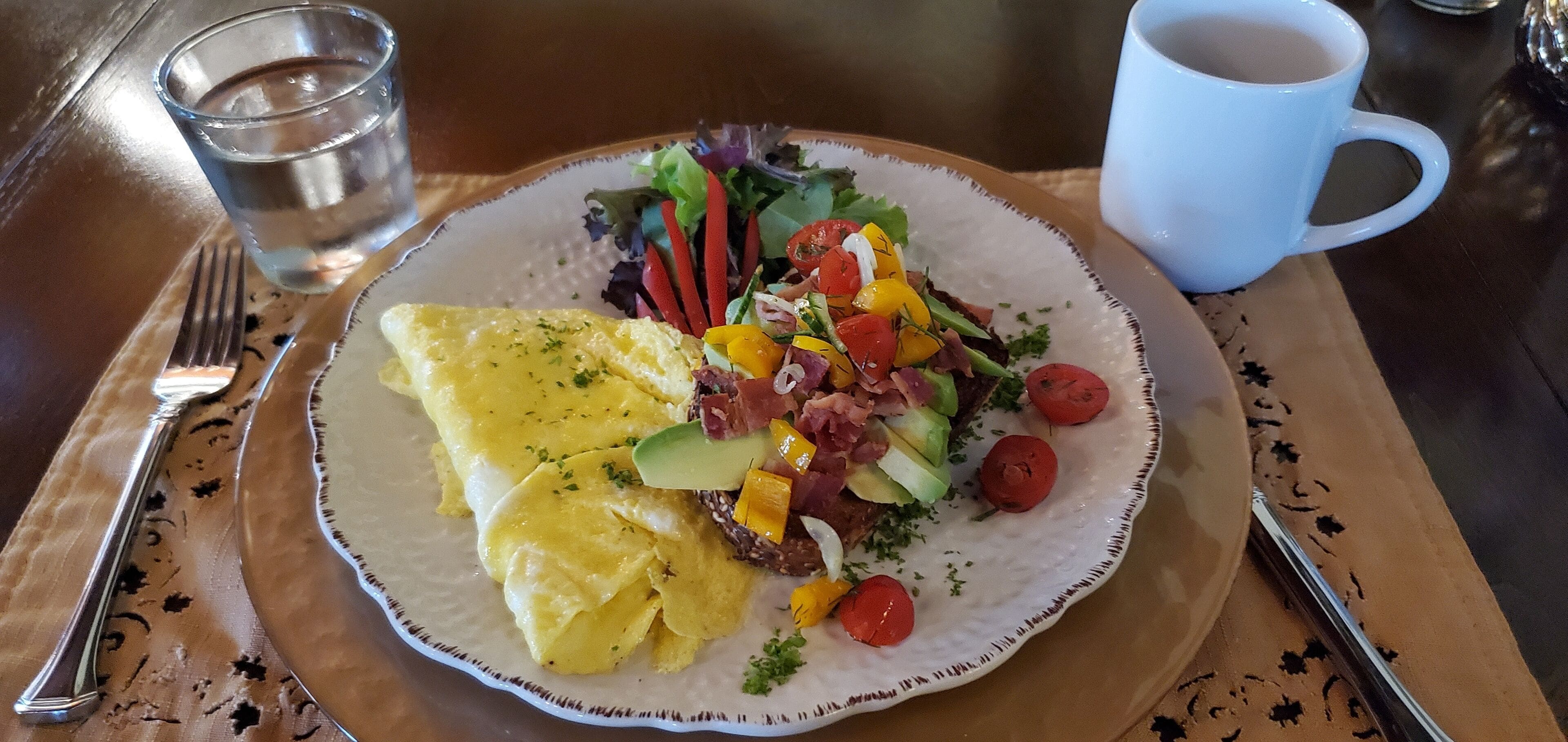 A plate of food with eggs, meat, and vegetables, a glass of water, and a coffee cup on a table.