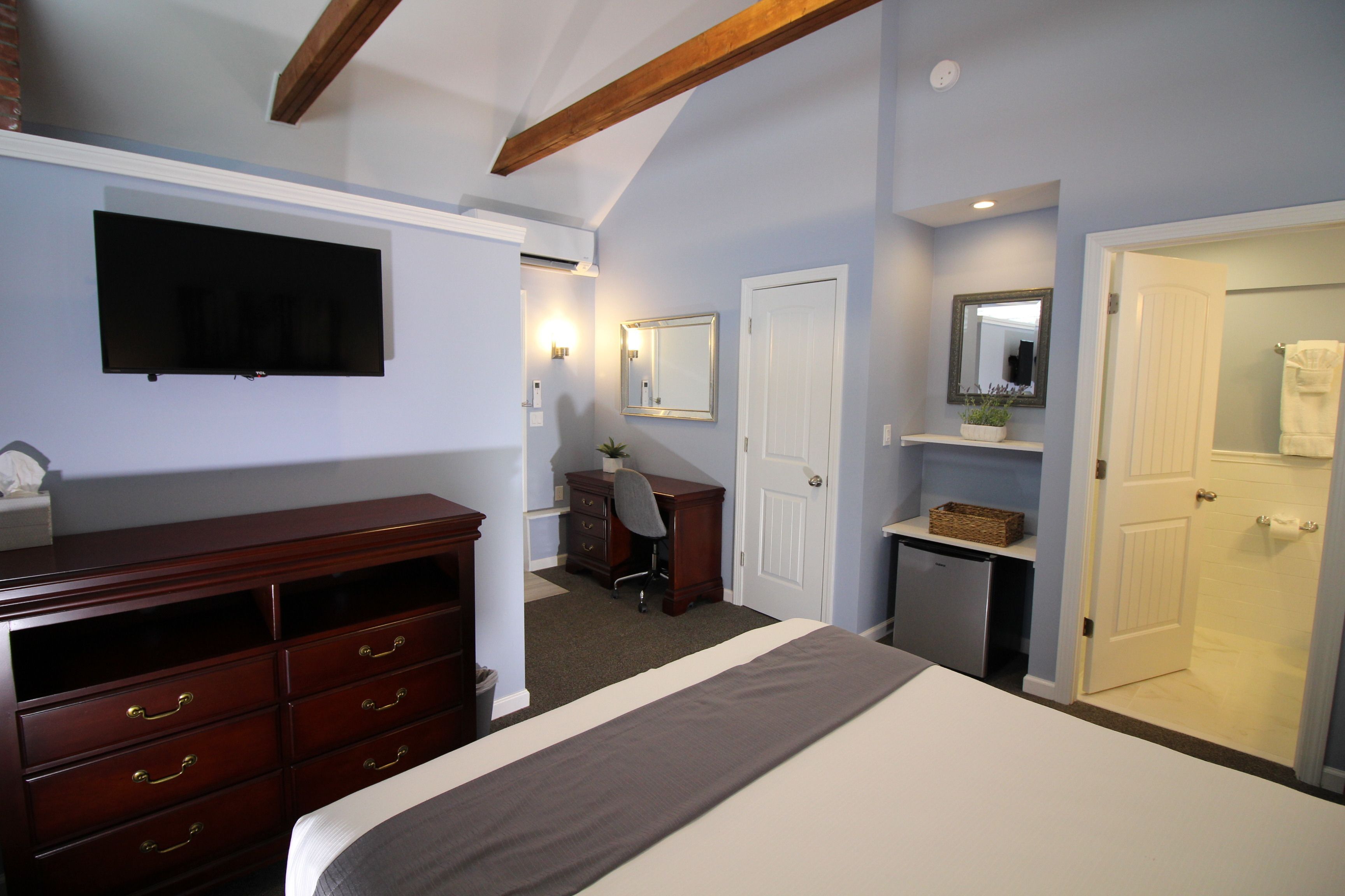 A bedroom with a bed, dresser, desk, chair, and a television mounted on the wall.