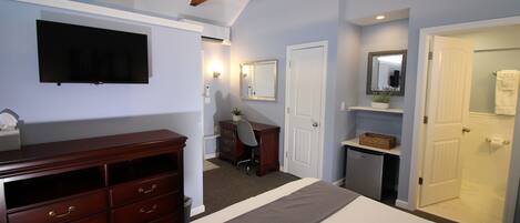 A bedroom with a bed, dresser, desk, chair, and a television mounted on the wall.