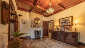 A spacious foyer with a wooden ceiling, a large chandelier, a fireplace, and a traditional wooden dresser with drawers. - Homestead Inn (New Milford)