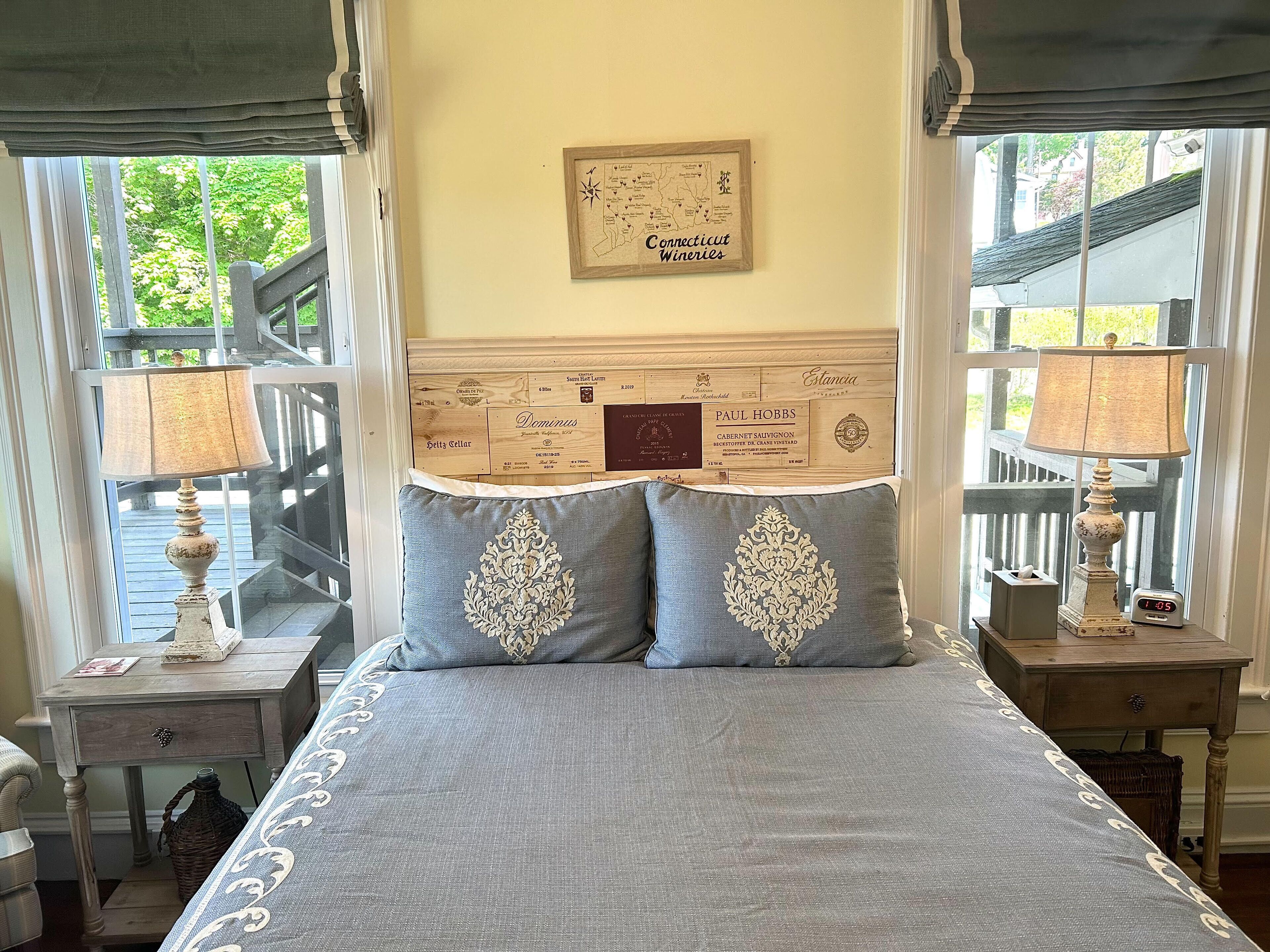 A bedroom with a bed, two nightstands, a map of Connecticut wineries on the headboard, and a window with a view of a deck.