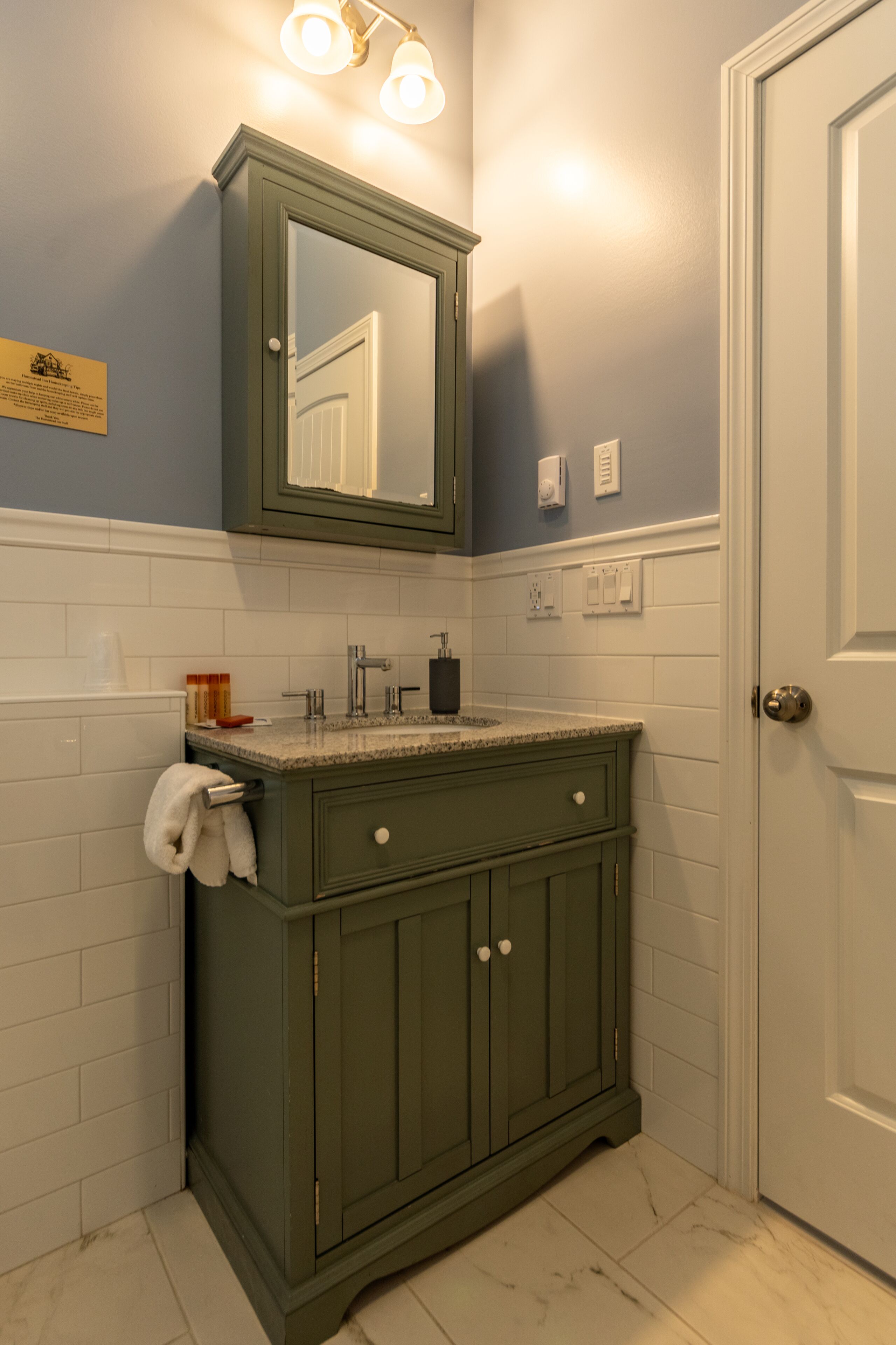 A bathroom with a green vanity, white tiles, a mirror, and a door.