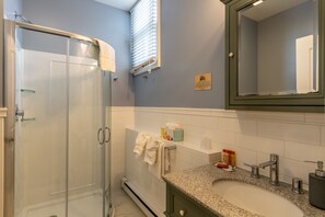 A bathroom with a glass shower enclosure, a sink with a granite countertop, and a mirror above the sink.