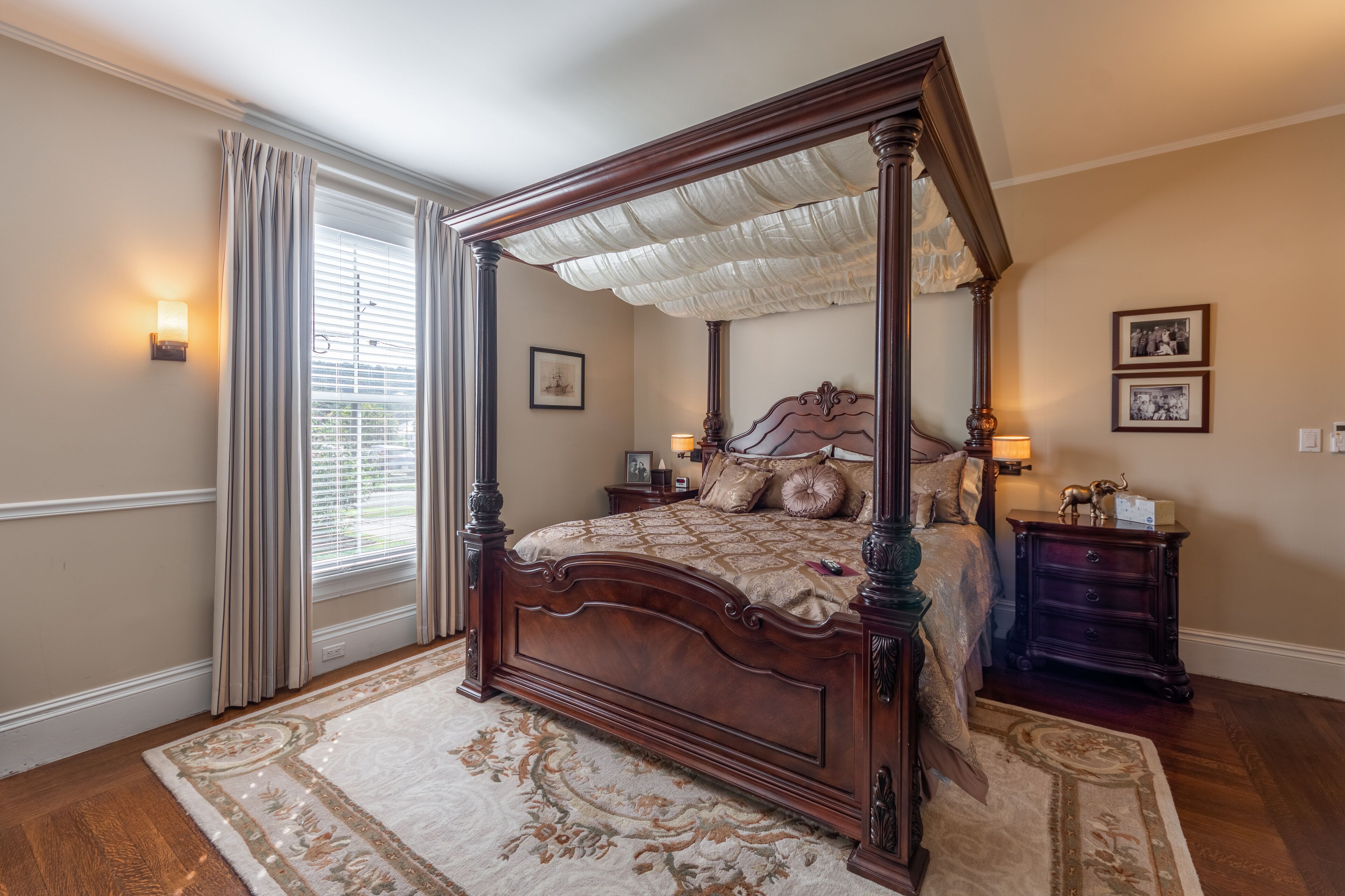 A four-poster bed with a canopy, a nightstand with a lamp, and a framed picture on the wall.