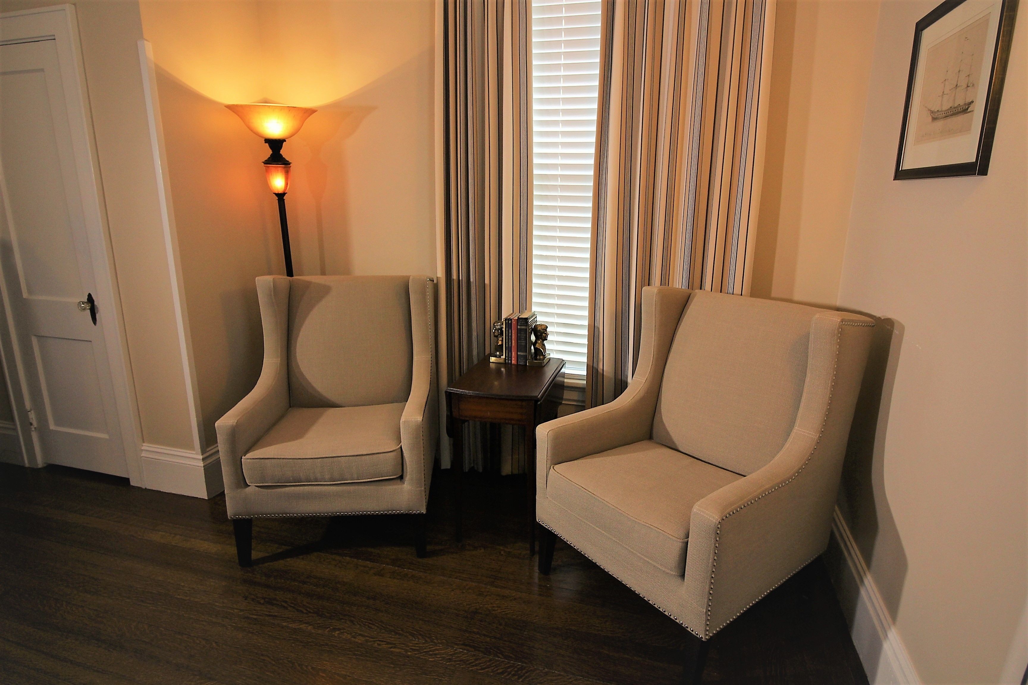 A room with two armchairs, a floor lamp, a small table with books, and a window with curtains.