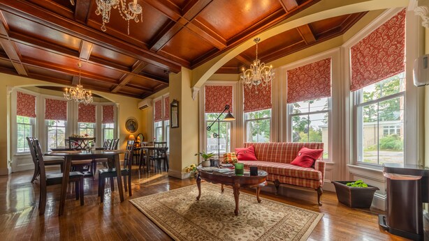 A spacious living room with hardwood floors, a large dining area, and a cozy seating area with a red sofa and matching cushions. - Homestead Inn (New Milford)