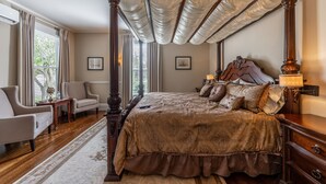 A four-poster bed with a canopy, a sitting area with a chair and a table, and a view of the outdoors through large windows. - Homestead Inn (New Milford)