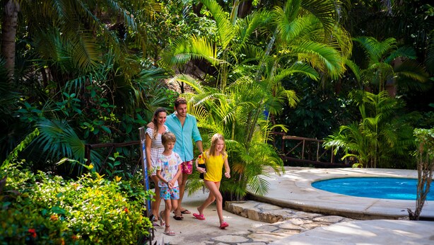 Une famille se dirige vers une zone de piscine, entourée d’une végétation luxuriante.