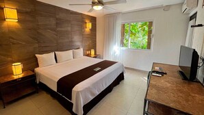 Une chambre d’hôtel avec un grand lit, des lampes de chevet, un bureau avec un ordinateur, un ventilateur de plafond et une fenêtre donnant sur un paysage verdoyant.