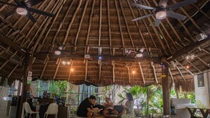 Un intérieur au toit de chaume, doté de ventilateurs de plafond, d’un comptoir d’accueil et d’espaces aménagés pour s’asseoir.