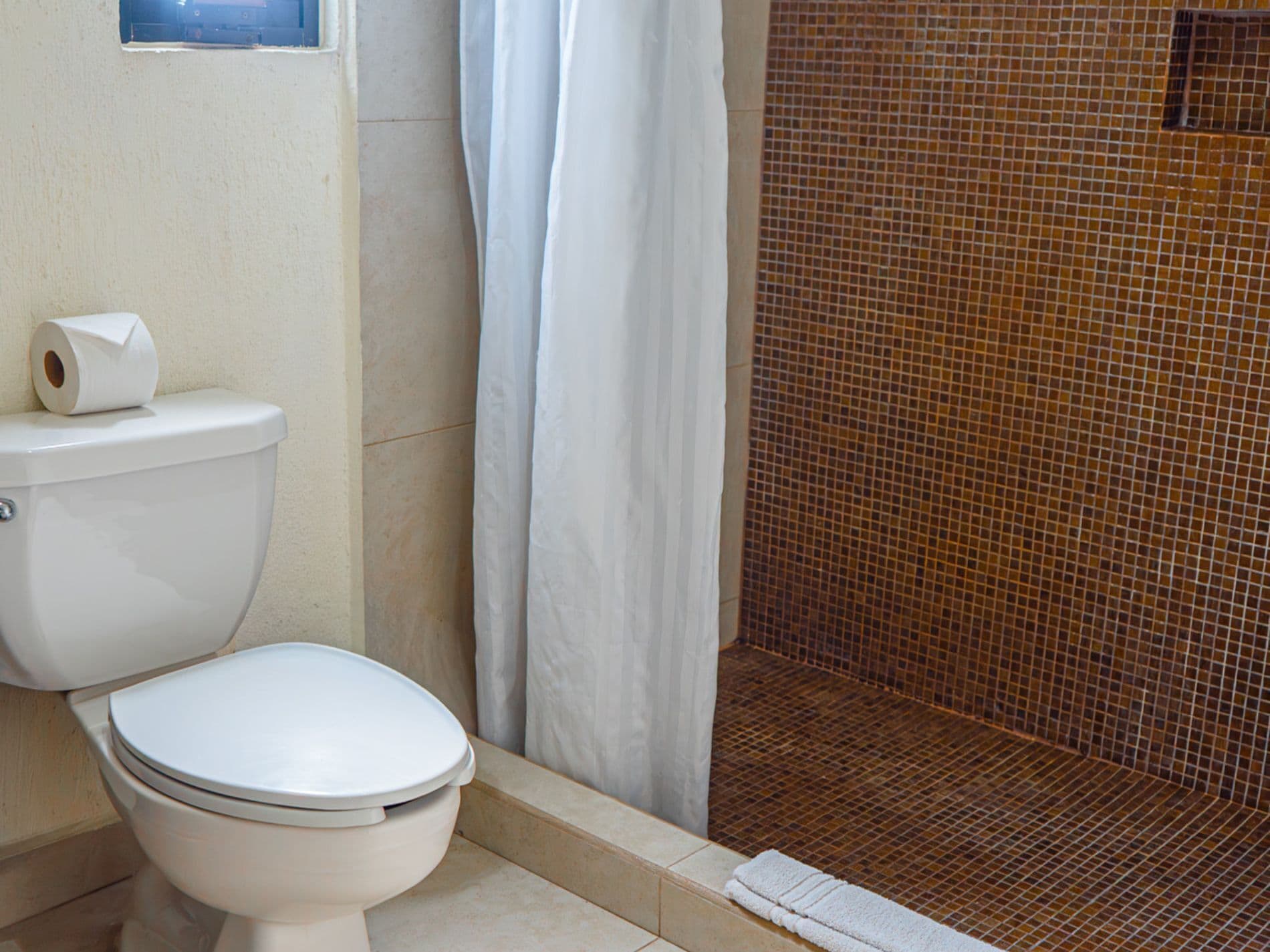 A bathroom with a toilet, a shower curtain, and a tiled shower area.