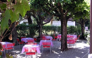 Un área de comedor al aire libre con mesas y sillas, rodeada de árboles y vegetación.