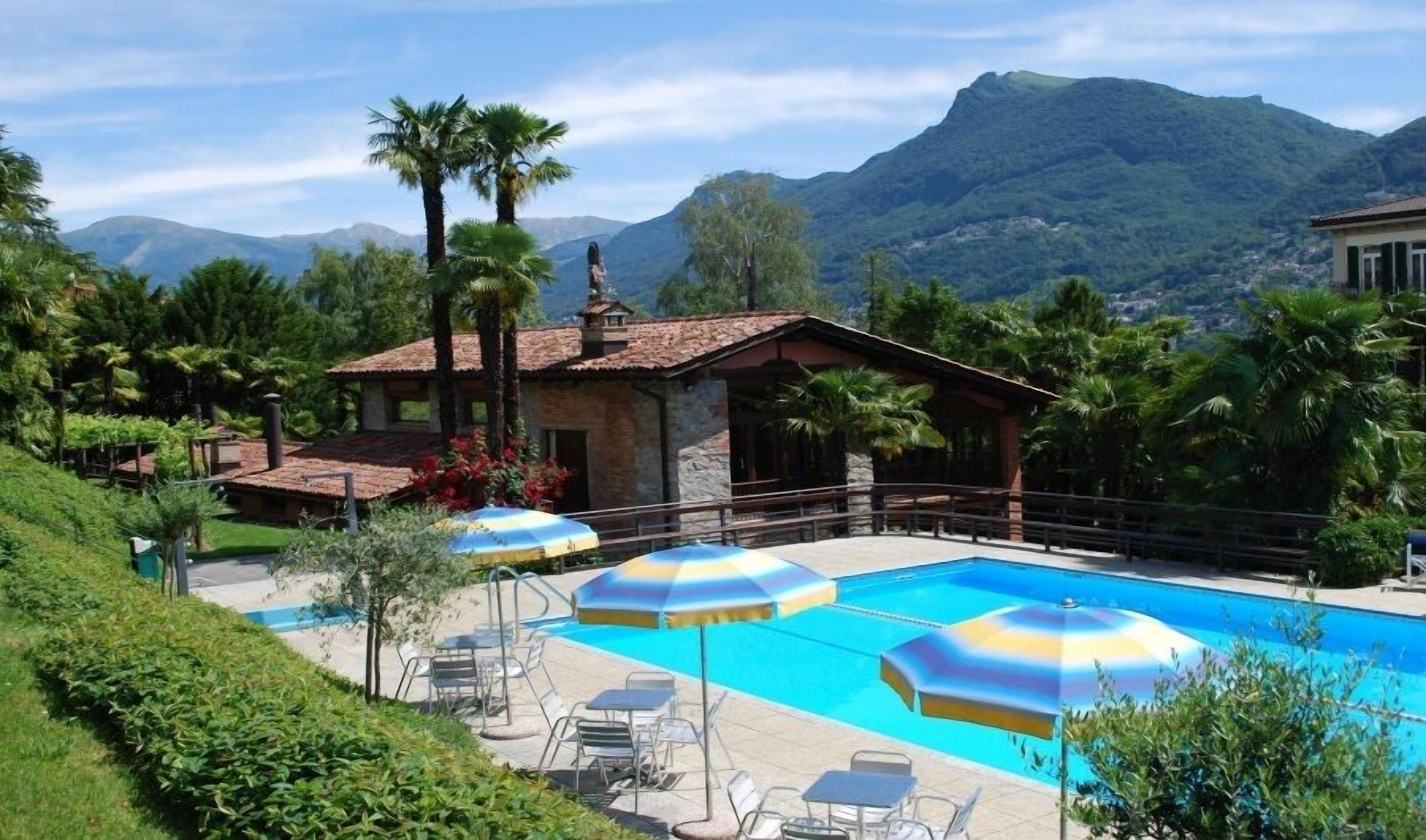 A pool area with umbrellas, lounge chairs, and a stone building with a tiled roof.