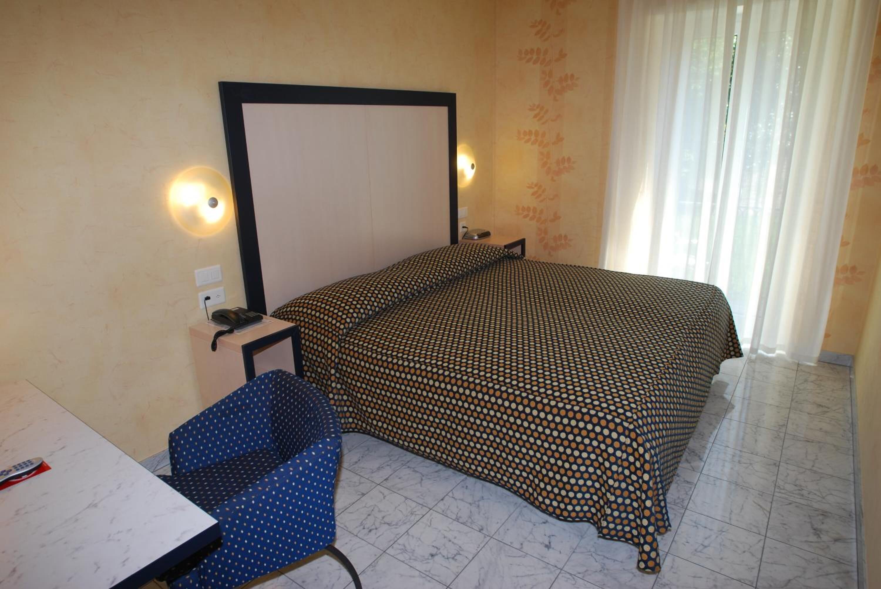A hotel room with a bed, a desk, a chair, and a window with curtains.