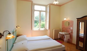 Une chambre avec deux lits, une fenêtre, un radiateur, un lavabo et un miroir.
