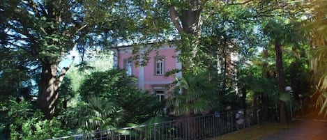 A pink building surrounded by lush greenery and a metal fence.