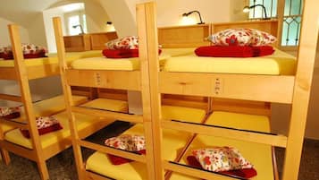Etagenbetten mit gelben Matratzen und blumigen Kissen, Holz-Kopfteile und ein kleiner Tisch mit einer Lampe.