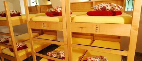 Bunk beds with yellow mattresses and floral pillows, wooden headboards, and a small table with a lamp.