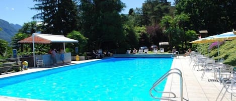 Una piscina rectangular con agua azul cristalina, rodeada por un solárium con baldosas, sillas de descanso y sombrillas.