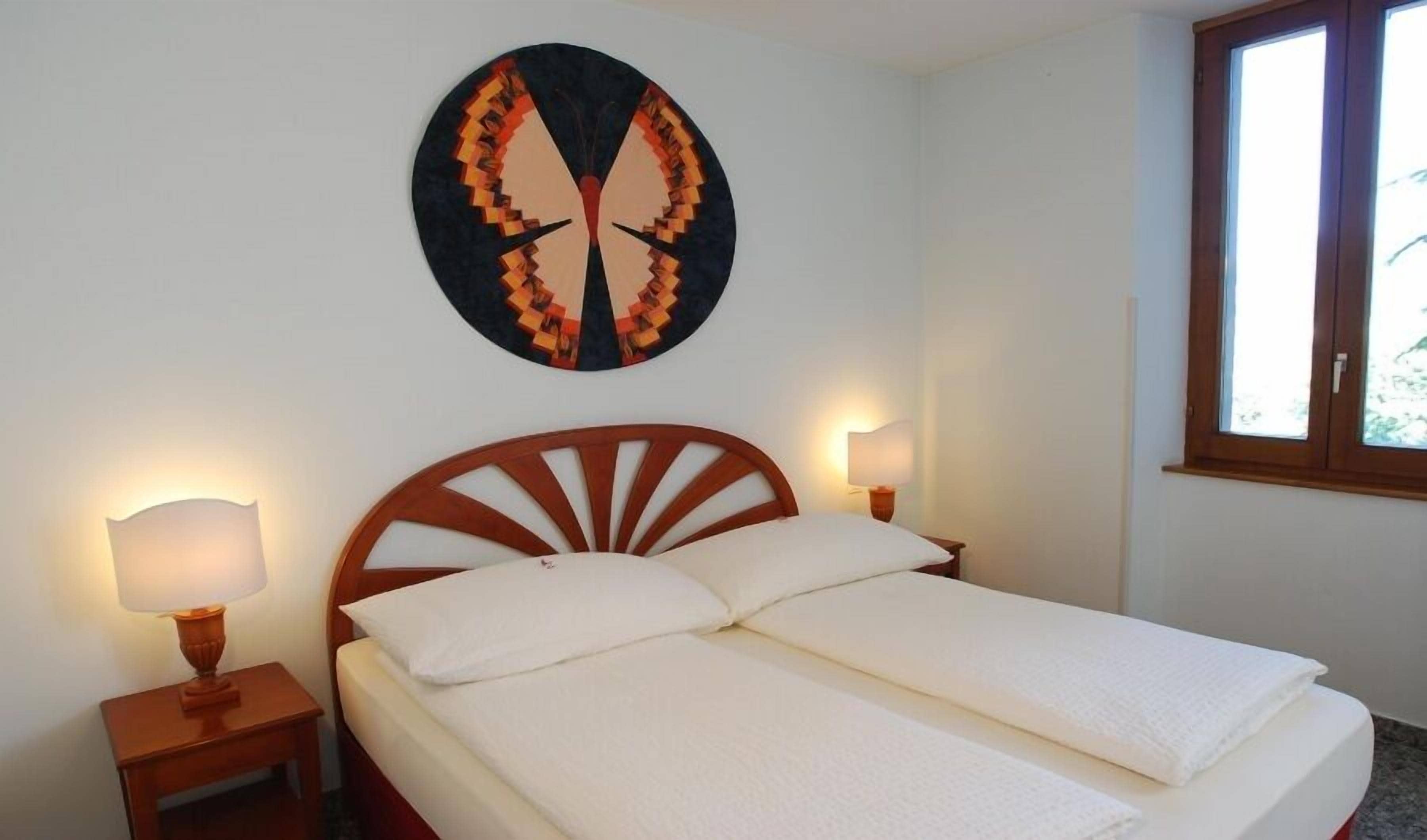 Un dormitorio con cama, dos lámparas de noche, una obra de arte en la pared y una ventana.