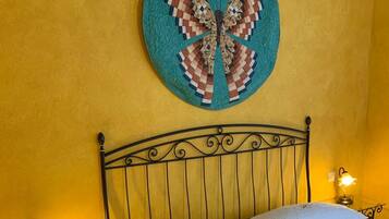 Una cama con colchón y almohadas blancas, cabecera de metal y una obra de arte circular colgada en la pared.