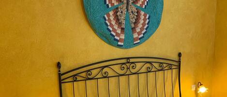 A bed with a white mattress and pillows, a metal headboard, and a wall-mounted circular artwork.