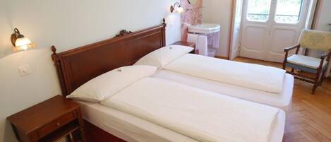 A double bed with a wooden headboard, a bedside table, a small bedside lamp, a mirror above the sink, and a chair near the window.