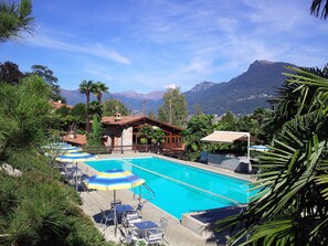 A swimming pool with lounge chairs and umbrellas, surrounded by tropical plants and a mountain view. - Hotel & Hostel Montarina (Lugano)
