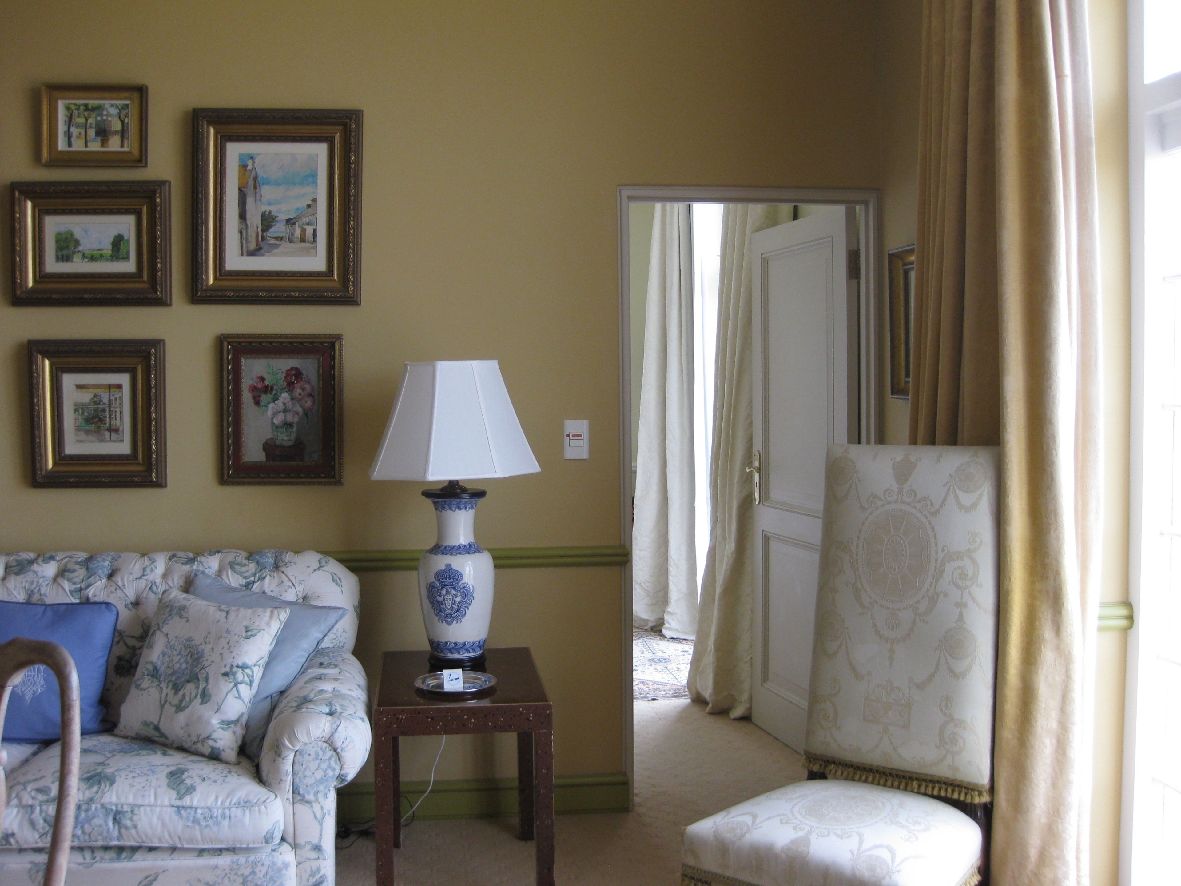 Una habitación con sofá, una silla, una mesa con lámpara y cuadros en la pared.