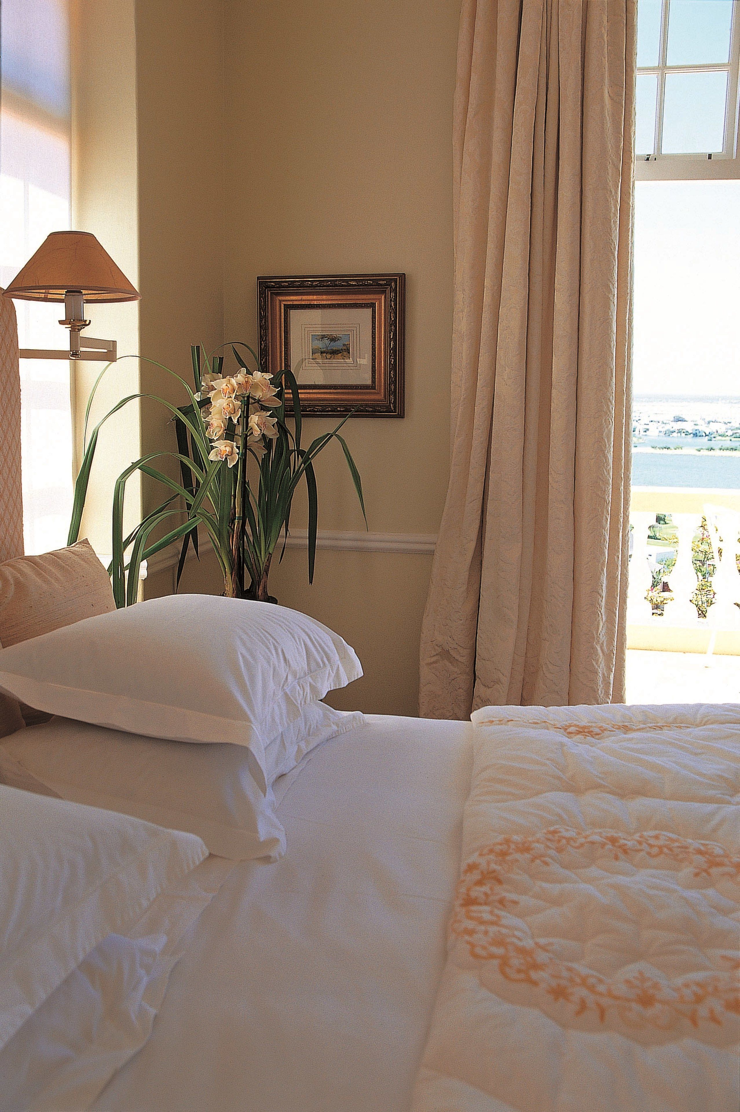 A hotel room with a bed, a lamp, a framed picture, and a view of the sea.