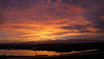 Um pôr do sol sobre a água, com o horizonte de uma cidade ao longe.
